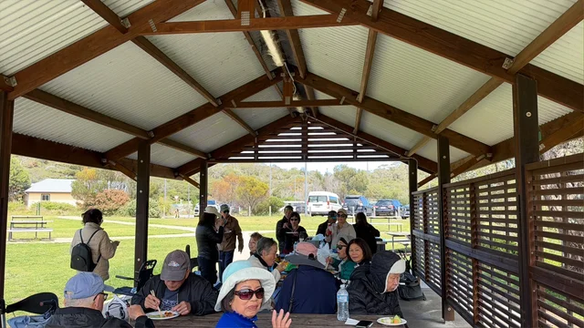Community members sharing lunch at picnic tables under an outdoor shelter